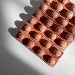 Overhead view of multiple handmade ceramic paintbrush holders in coral red finish tightly packed in a row.