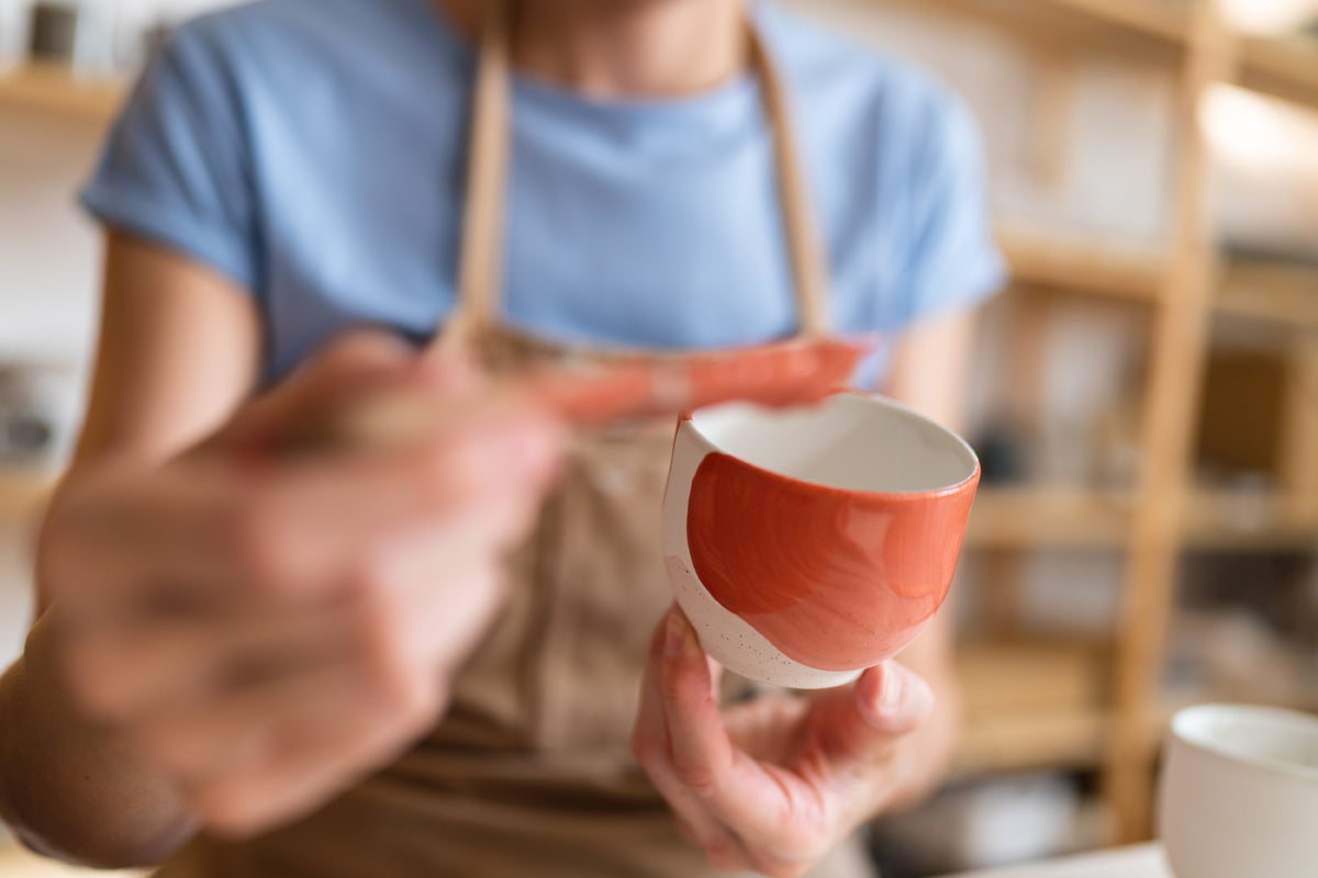 Applying glaze to a handmade ceramic cup using a brush.