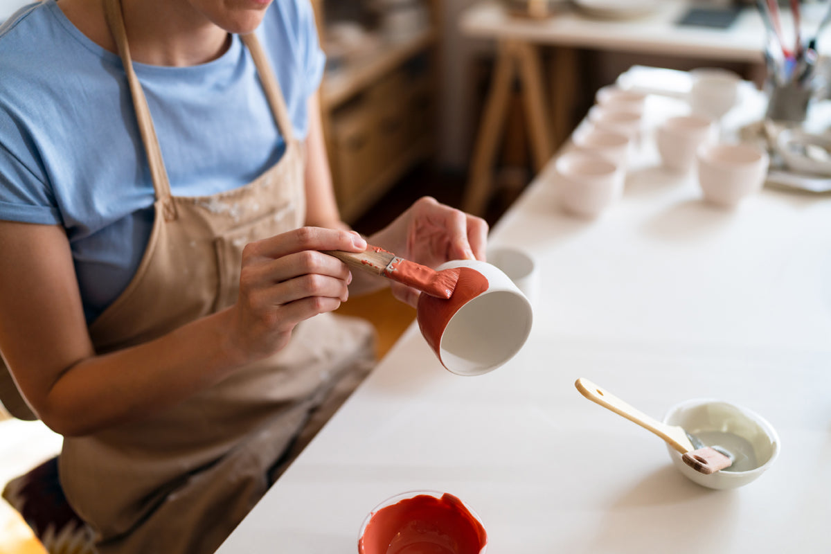 Applying glaze to a handmade ceramic cup using a brush.
