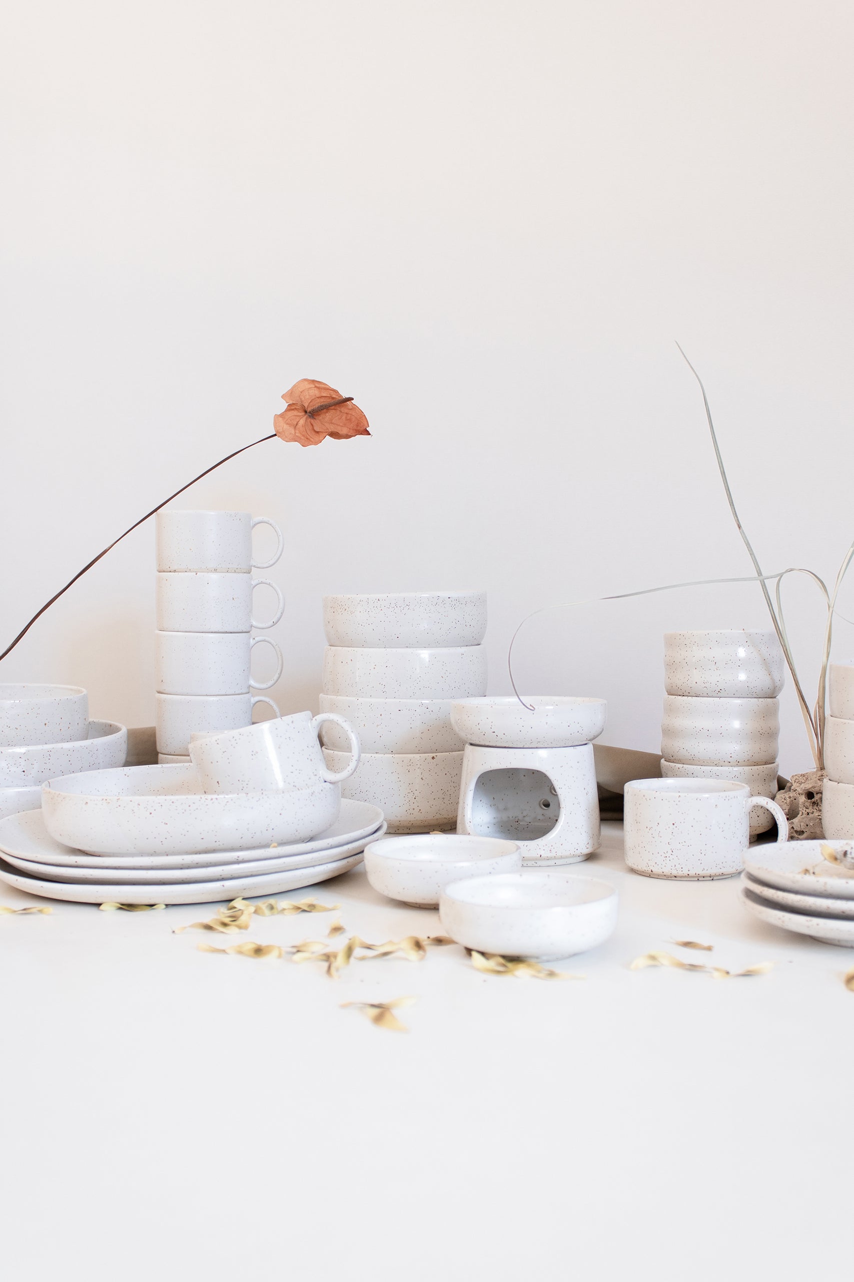 An assortment of artisanal tableware by Made of Dust Ceramics, crafted in speckled white finish, arranged against white backdrop.