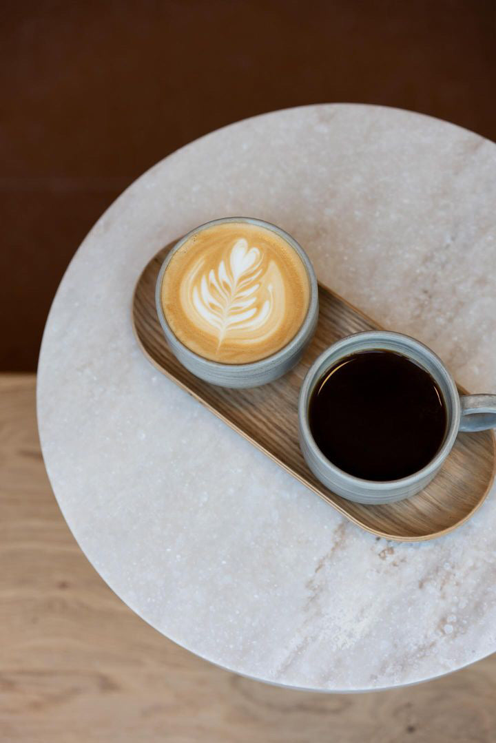 Overhead view of two Sand coffee cups containing coffee set at a round marble table top.