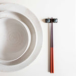 Handcrafted midnight blue chopstick rest with wooden chopsticks, placed next to a speckled white dining set.