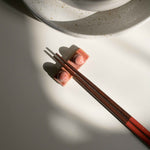 Handcrafted coral red chopstick rest with wooden chopsticks, placed next to a speckled white dining set.