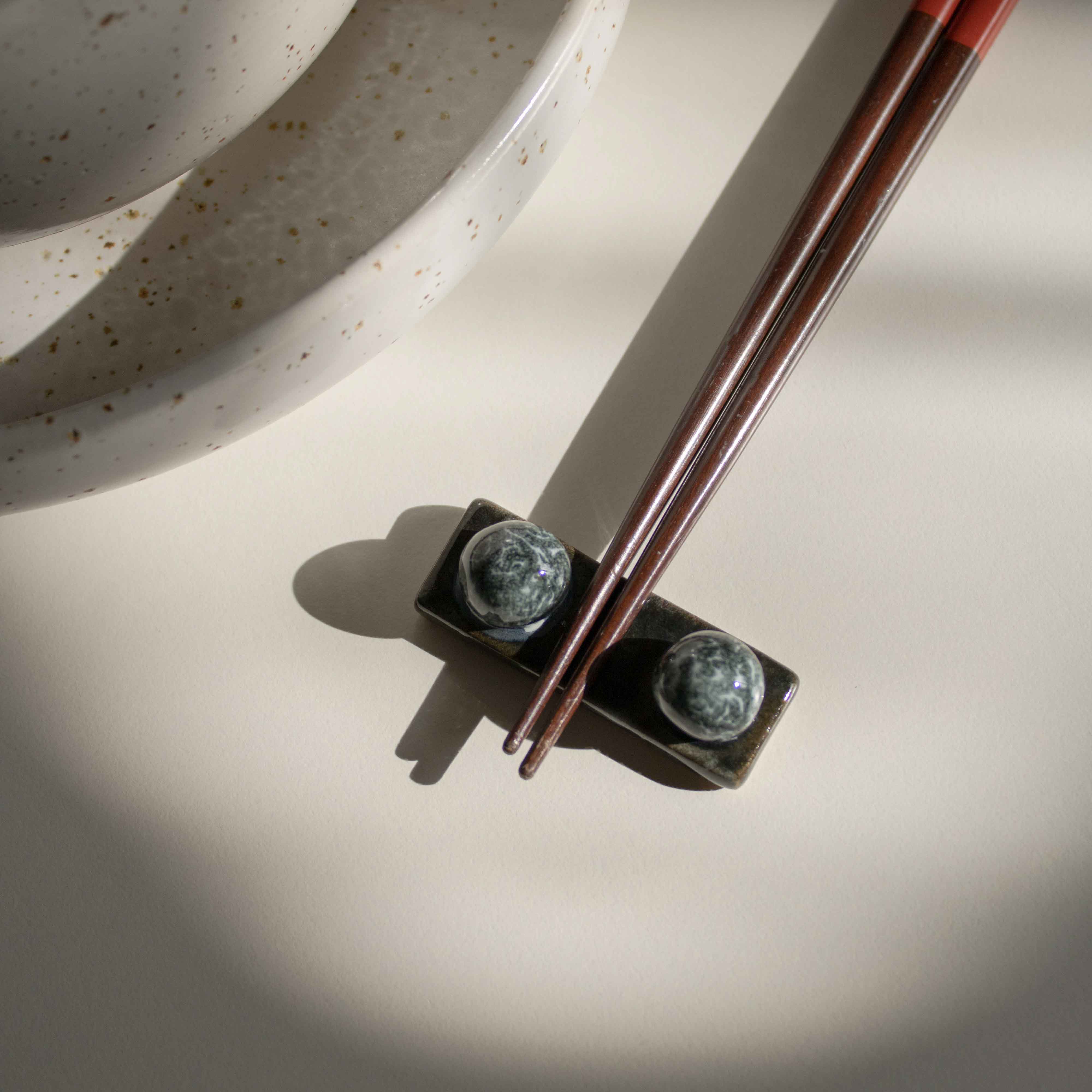 Handcrafted midnight blue chopstick rest with wooden chopsticks, placed next to a speckled white dining set.