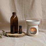 Handcrafted essential oil burner with a lit candle inside, displayed alongside glass oil bottles.