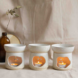 A group of three handcrafted essential oil burners with candles lit inside, displayed on a beige linen cloth.