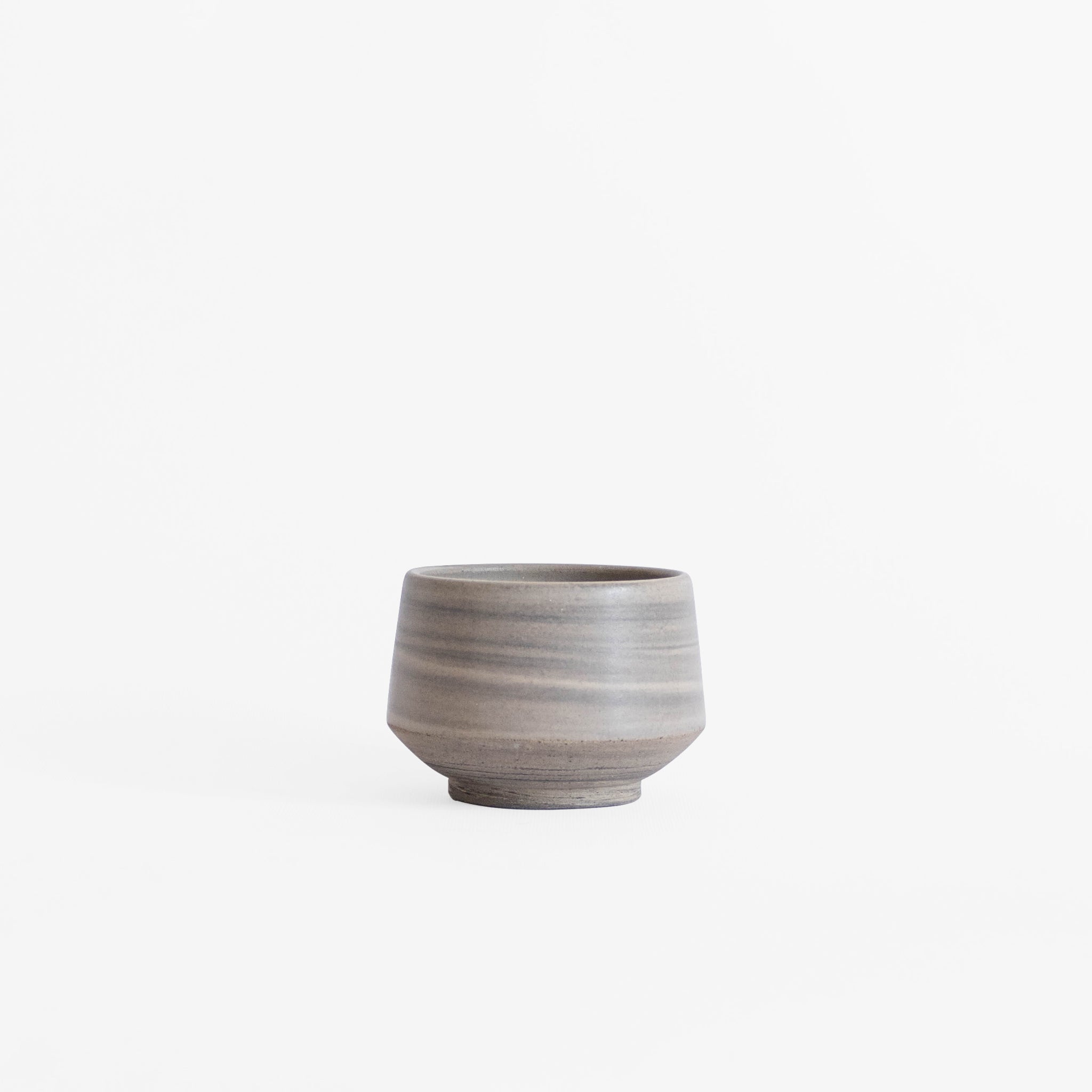 Handcrafted ceramic cup in natural earthy tones displayed against a white background.