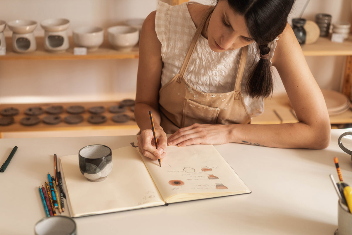 A ceramic artist sketching and planning designs in the pottery studio.