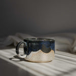 A handcrafted ceramic mug in rich deep blue tones, illuminated by a beam of light.