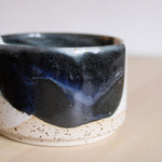 A close-up of a handmade ceramic cup, featuring glaze layering detail of deep blue and white glaze.