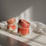 Stacks of handcrafted espresso cups in coral red finish, illuminated by contrasting light and shadows.