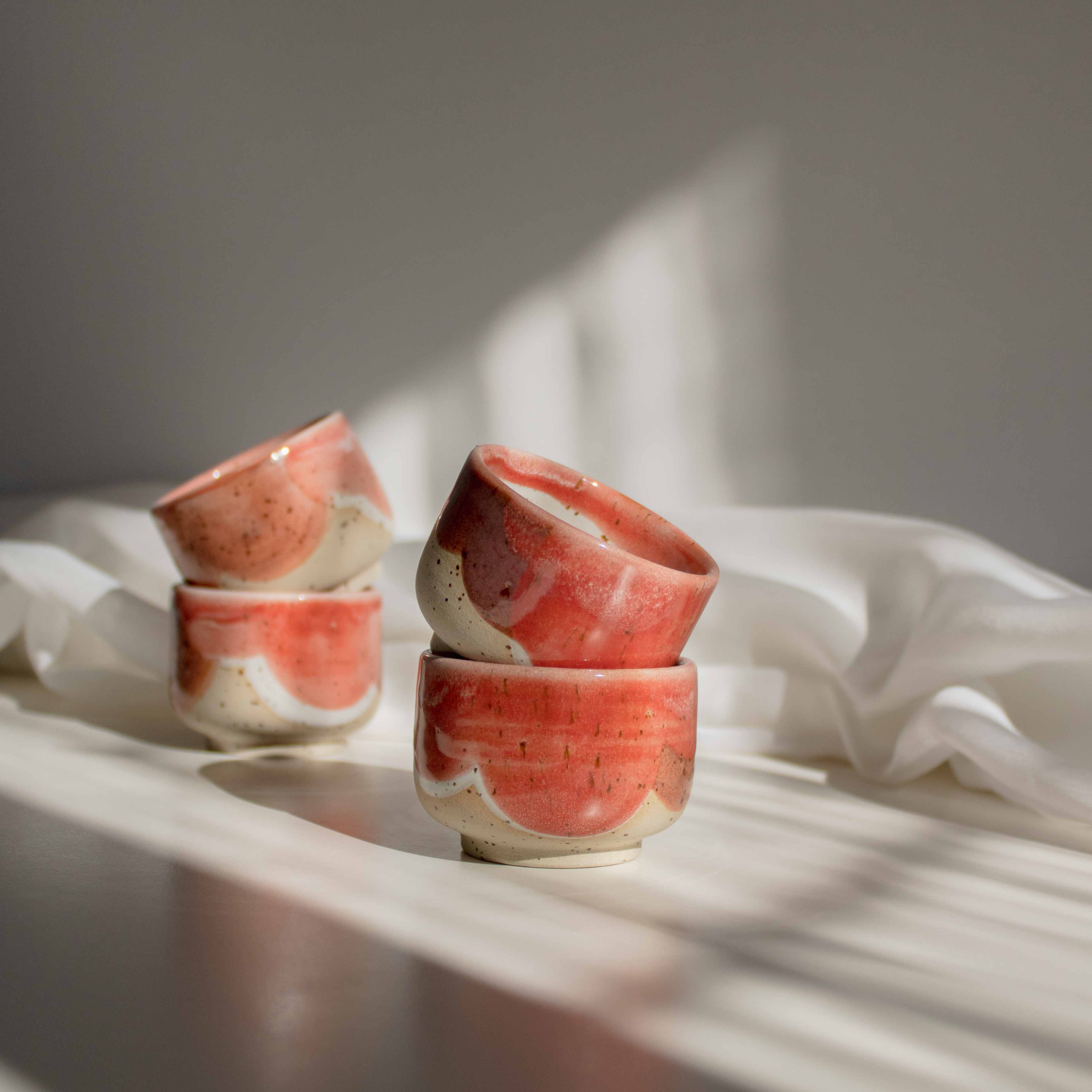 Stacks of handcrafted espresso cups in coral red finish, illuminated by contrasting light and shadows.