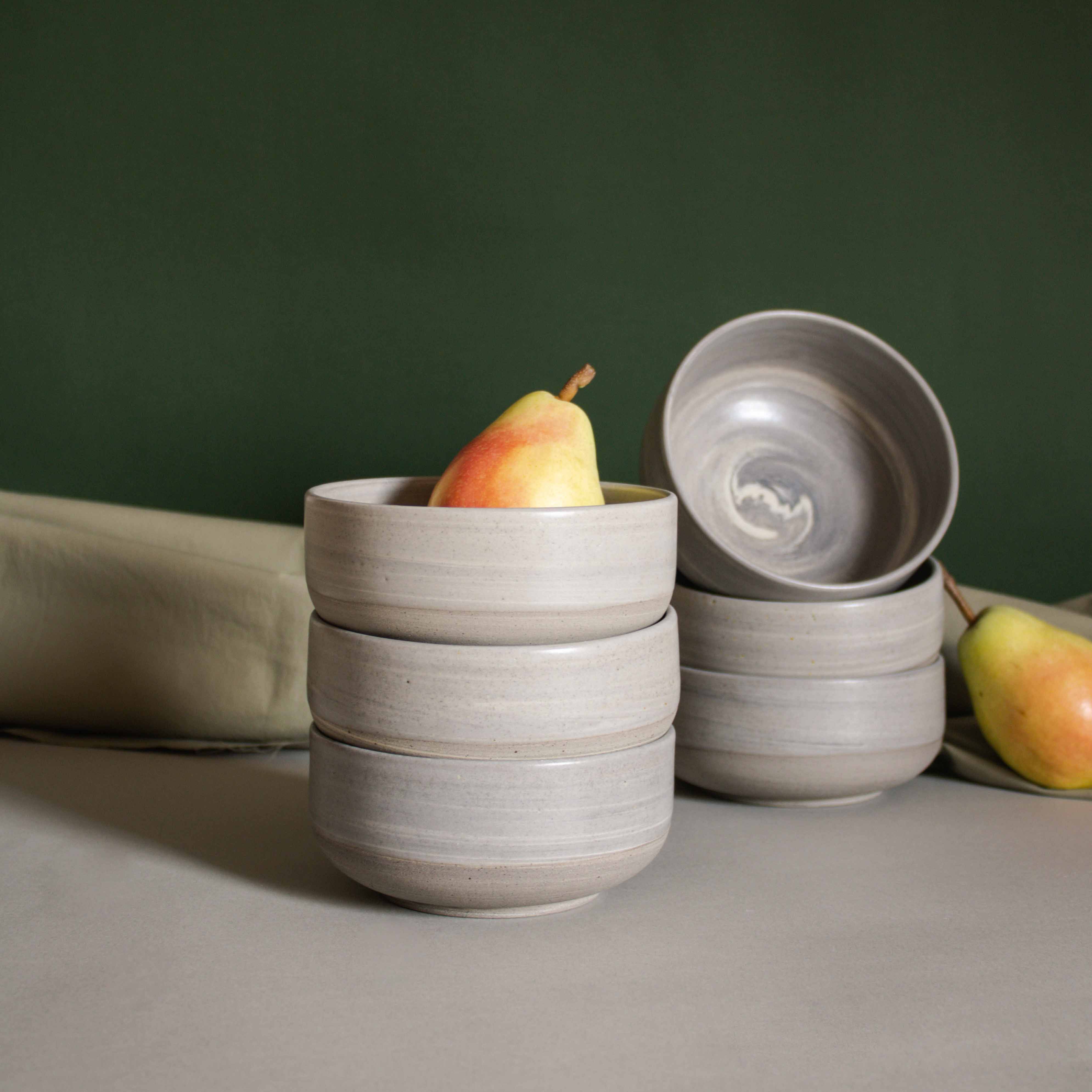 Elegant table setup featuring handmade ceramic bowls in earthy tones, accompanied by fresh pears and draped fabric.
