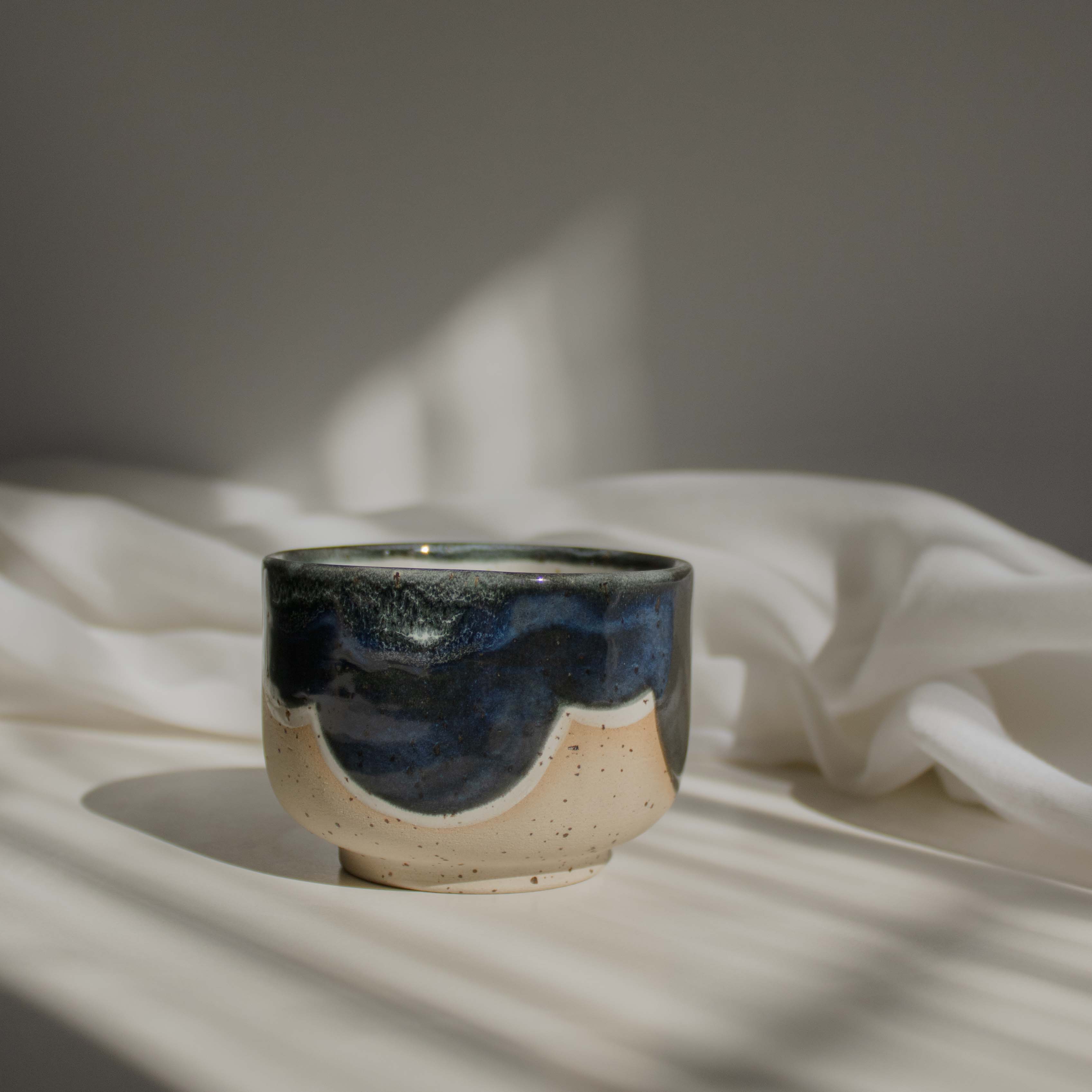 Close up of a handcrafted ceramic cup made of speckled cream clay, featuring rich melting glaze details in blue.