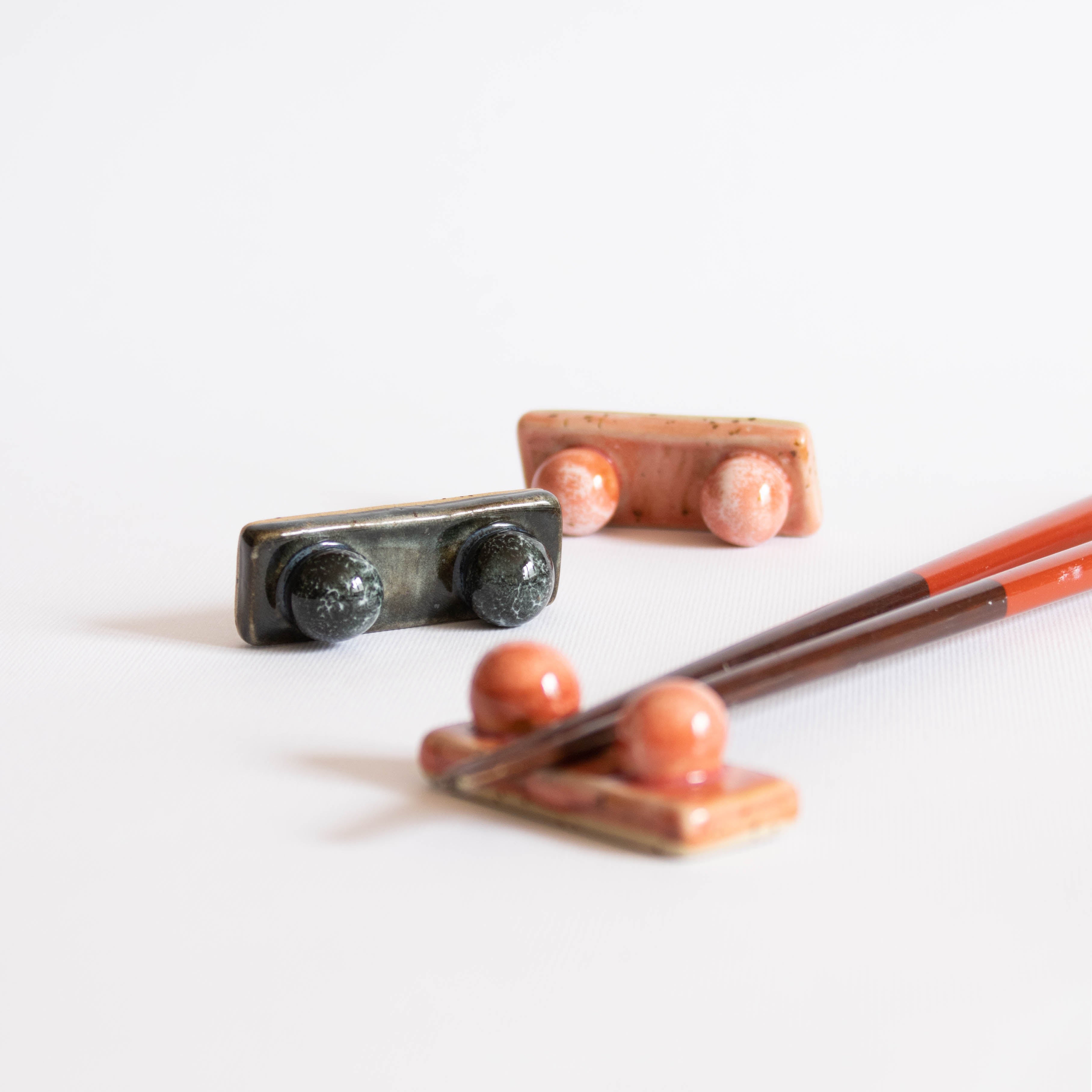 Handcrafted midnight blue and coral red chopstick rest with wooden chopsticks displayed on a white surface.