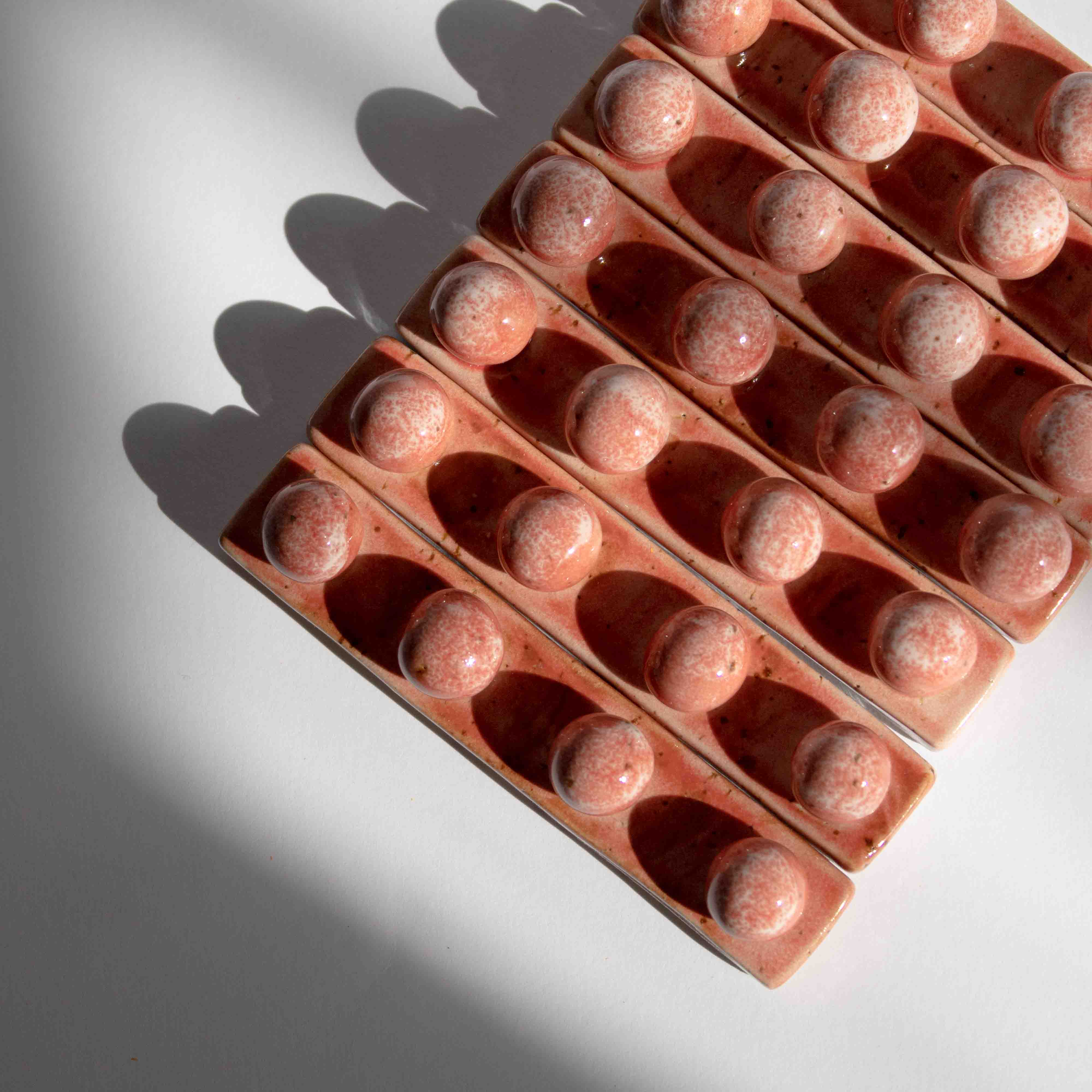 Overhead view of multiple handmade ceramic paintbrush holders in coral red finish tightly packed in a row.
 