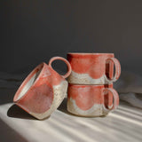 Group of coral red cups with handles illuminated by a beam of light.