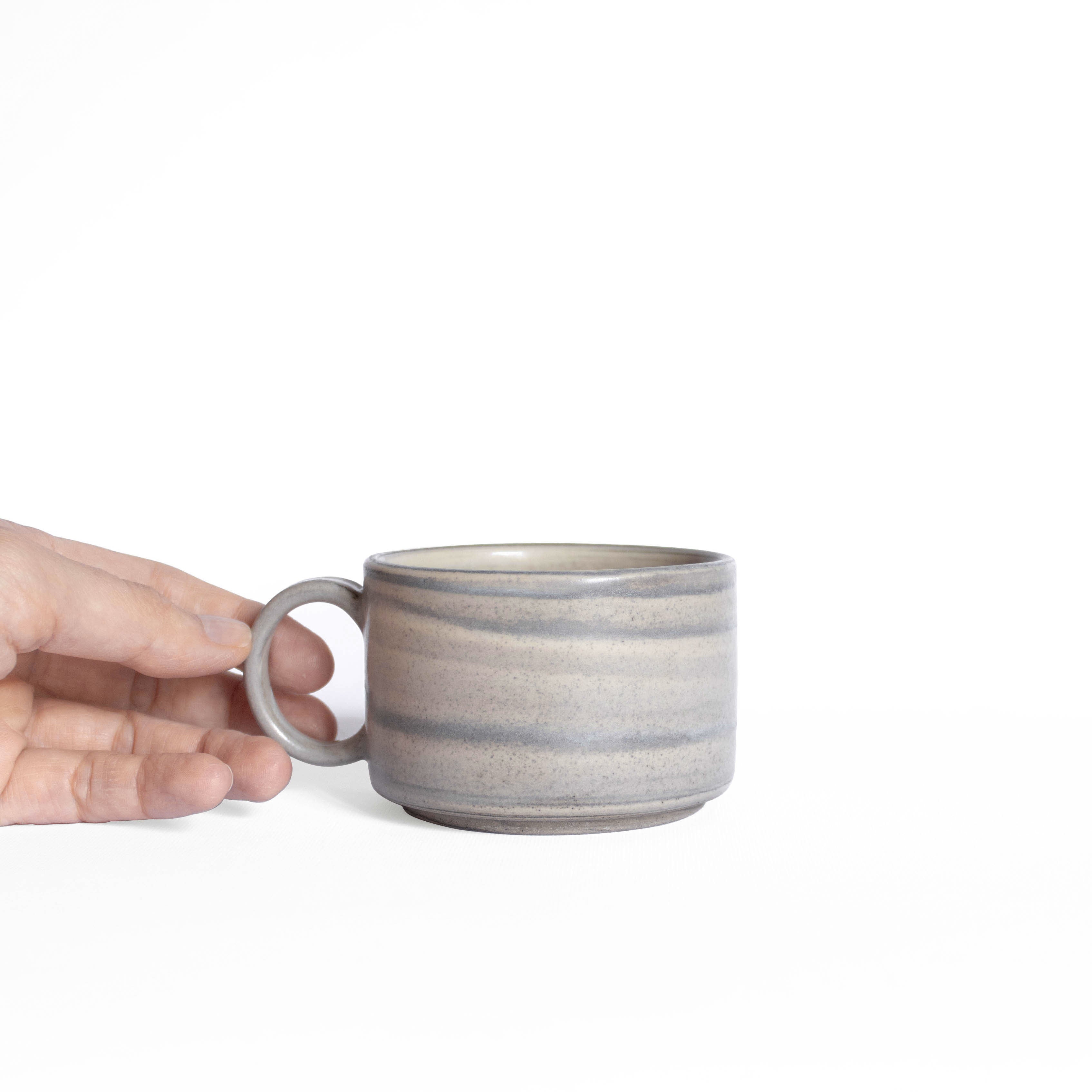 Handmade ceramic cup with handle in natural earthy tones, held in hand for a closer look.