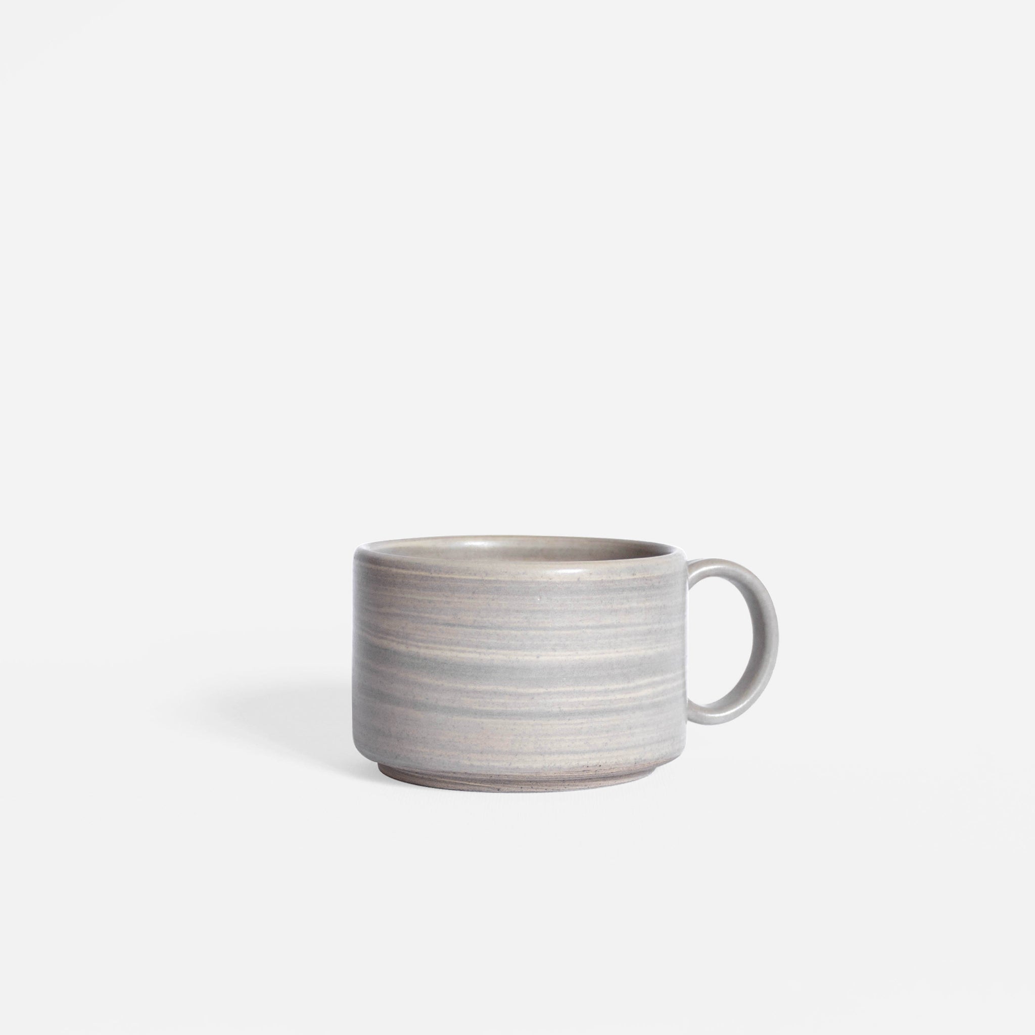 Handmade ceramic coffee cup with handle in earthy tones, showcased against a white backdrop.