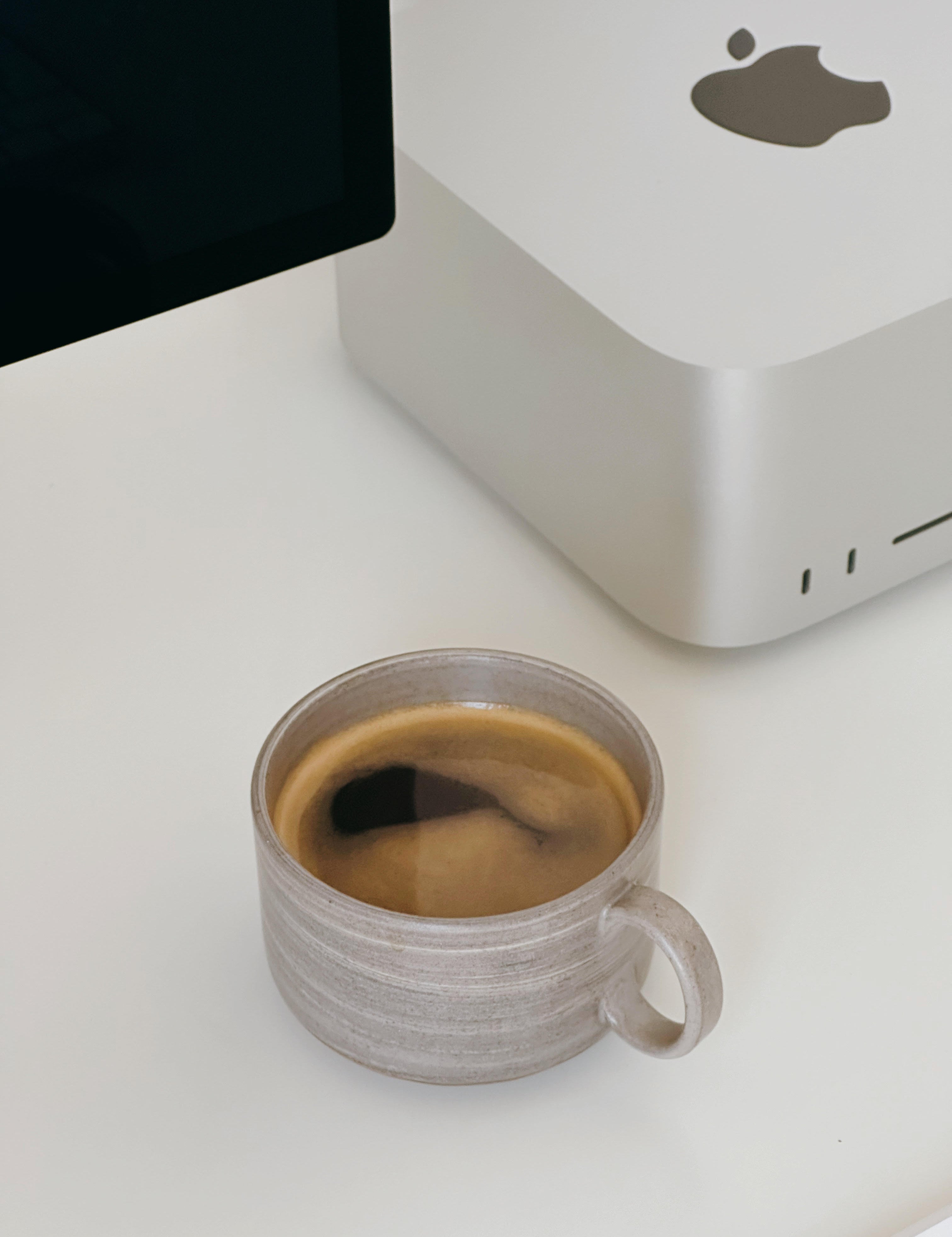 Handmade gray ceramic mug placed on a white table next to a computer monitor.