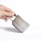 Handmade ceramic cup with handle in natural earthy tones, held in hand for a closer look.