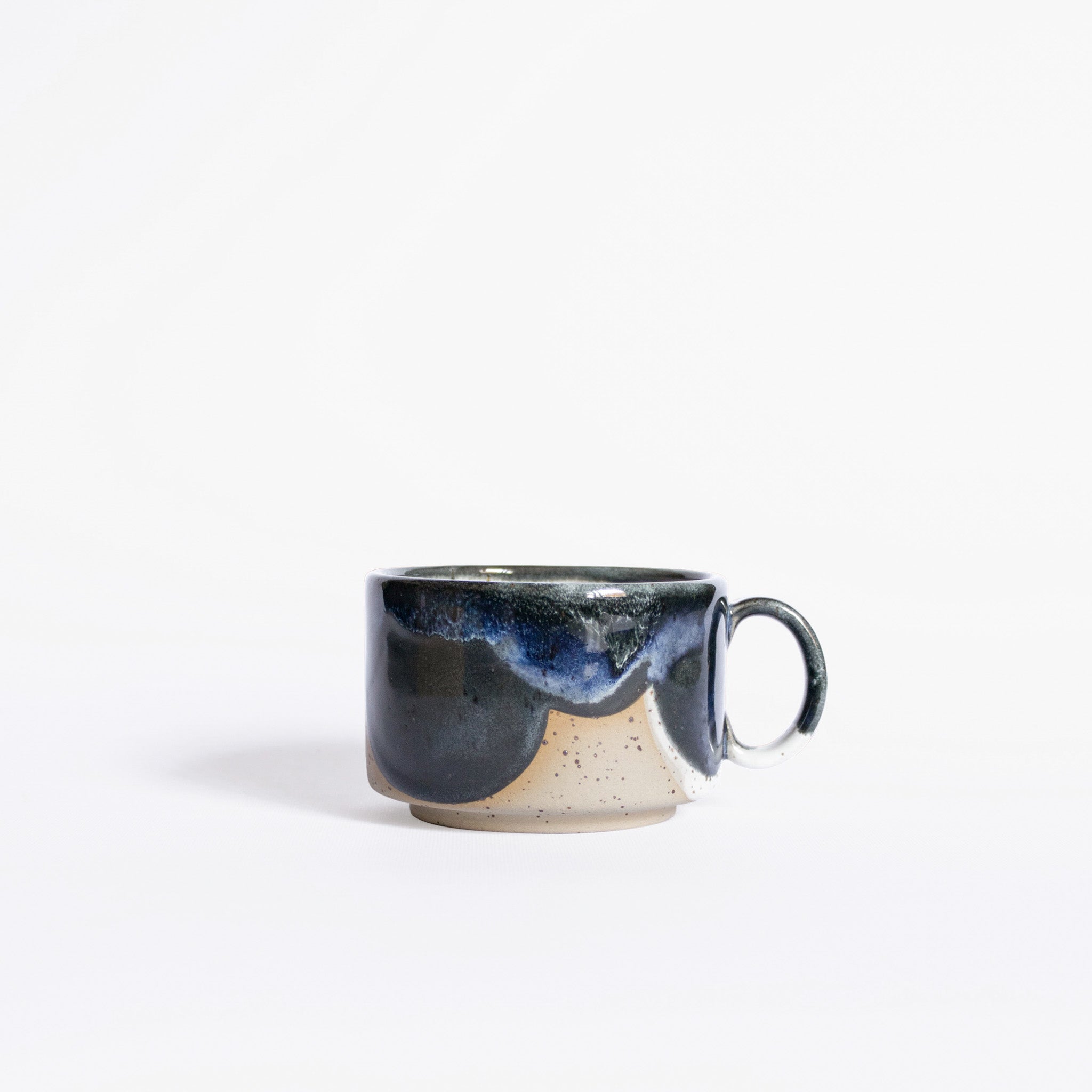 A handcrafted ceramic cup with a handle, displaying a lively organic glaze pattern in deep blue and white finishes, showcased against a pristine white background.