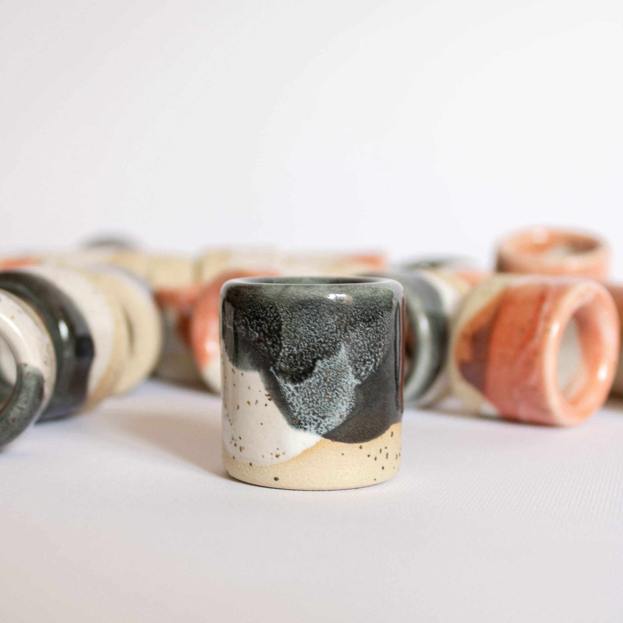 Foregrounded handmade ceramic toothbrush or pen holder in a blue finish, against a backdrop of blurred holders scattered in the background.