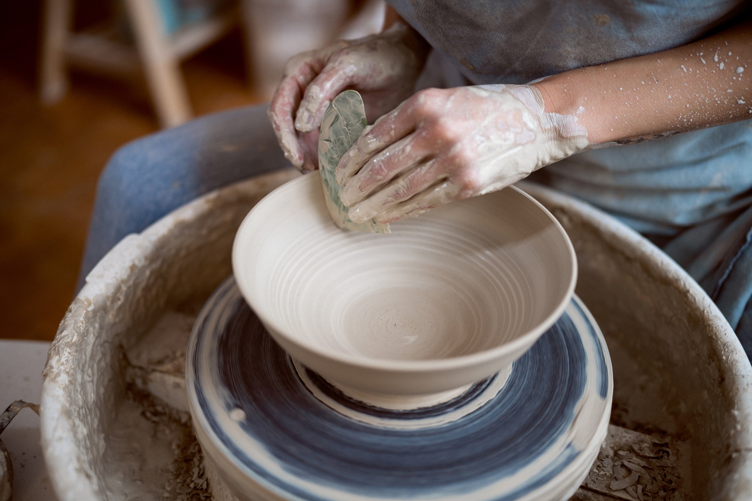 Hands crafting a ceramic bowl on a pottery wheel with the aid of a pottery rib.