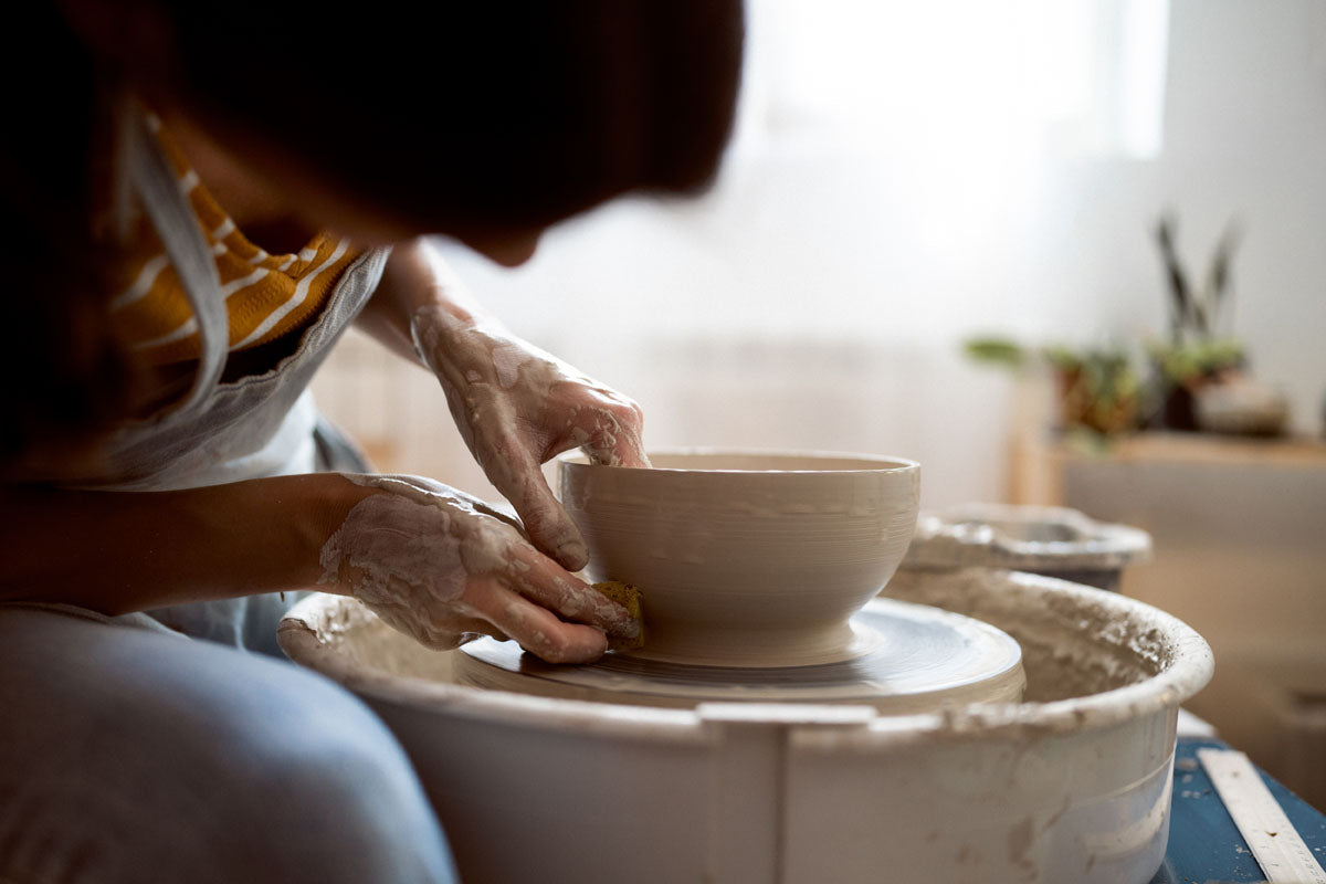 A side perspective of a ceramist shaping a ceramic bowl on the potter's wheel.