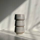 A stack of three handcrafted ceramic cups in natural earthy tones.