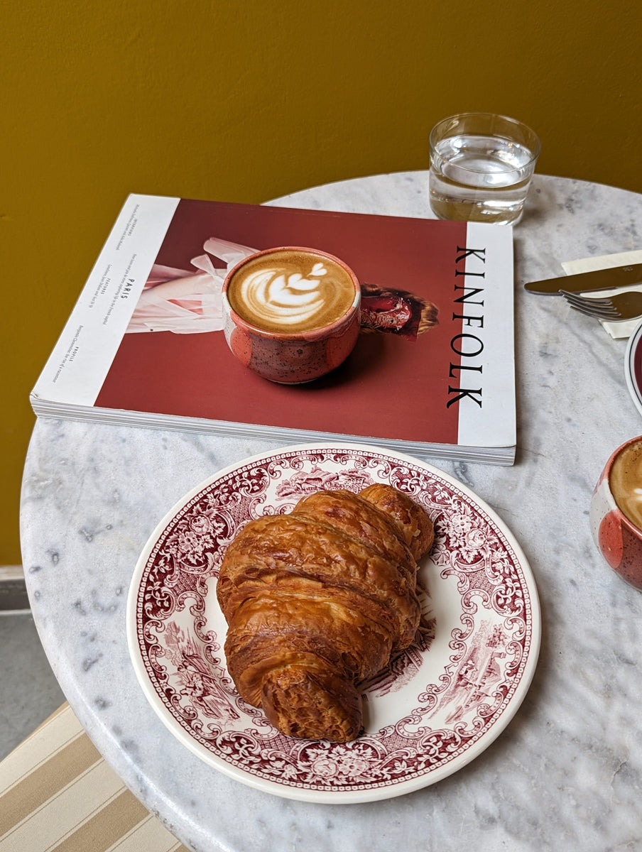 A coral red handmade ceramic cup placed atop a magazine cover on a round marble tabletop.