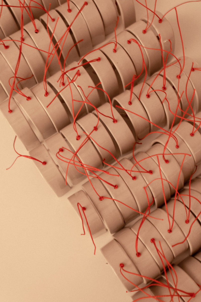 An overhead view of multiple Christmas ornaments, each with red thread, arranged in lines and rows on the tabletop.