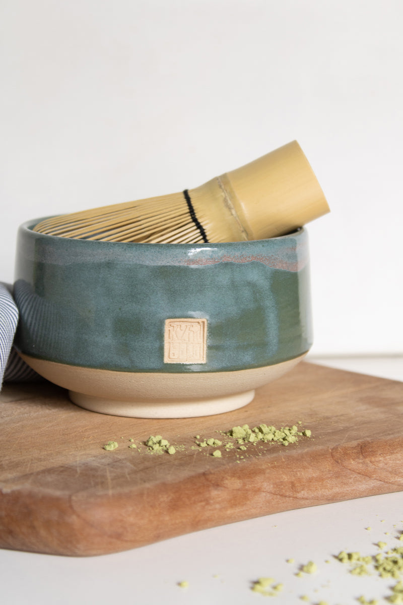 A handcrafted ceramic matcha bowl in tourmaline green, accompanied by a matcha whisk nestled inside.