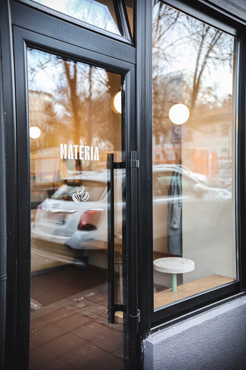 Black-framed entrance door of a specialty coffee shop displaying the shop's logo on the glass.