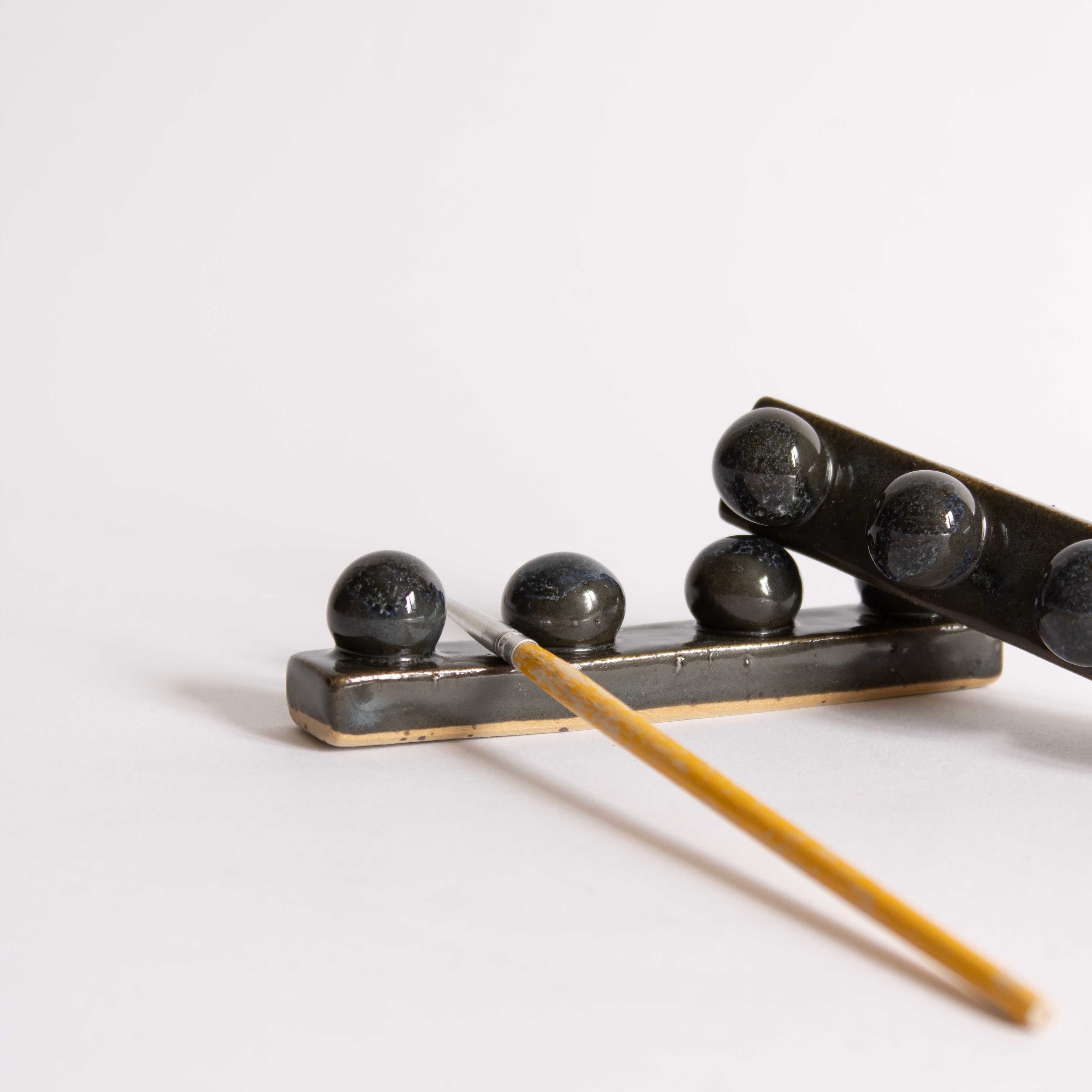 Side view of a handmade ceramic paintbrush holder in dark blue finish, holding a paintbrush.