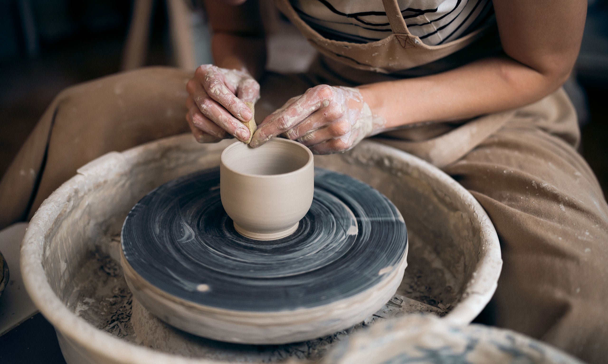 Craftsman shaping a ceramic cup on a potter's wheel.