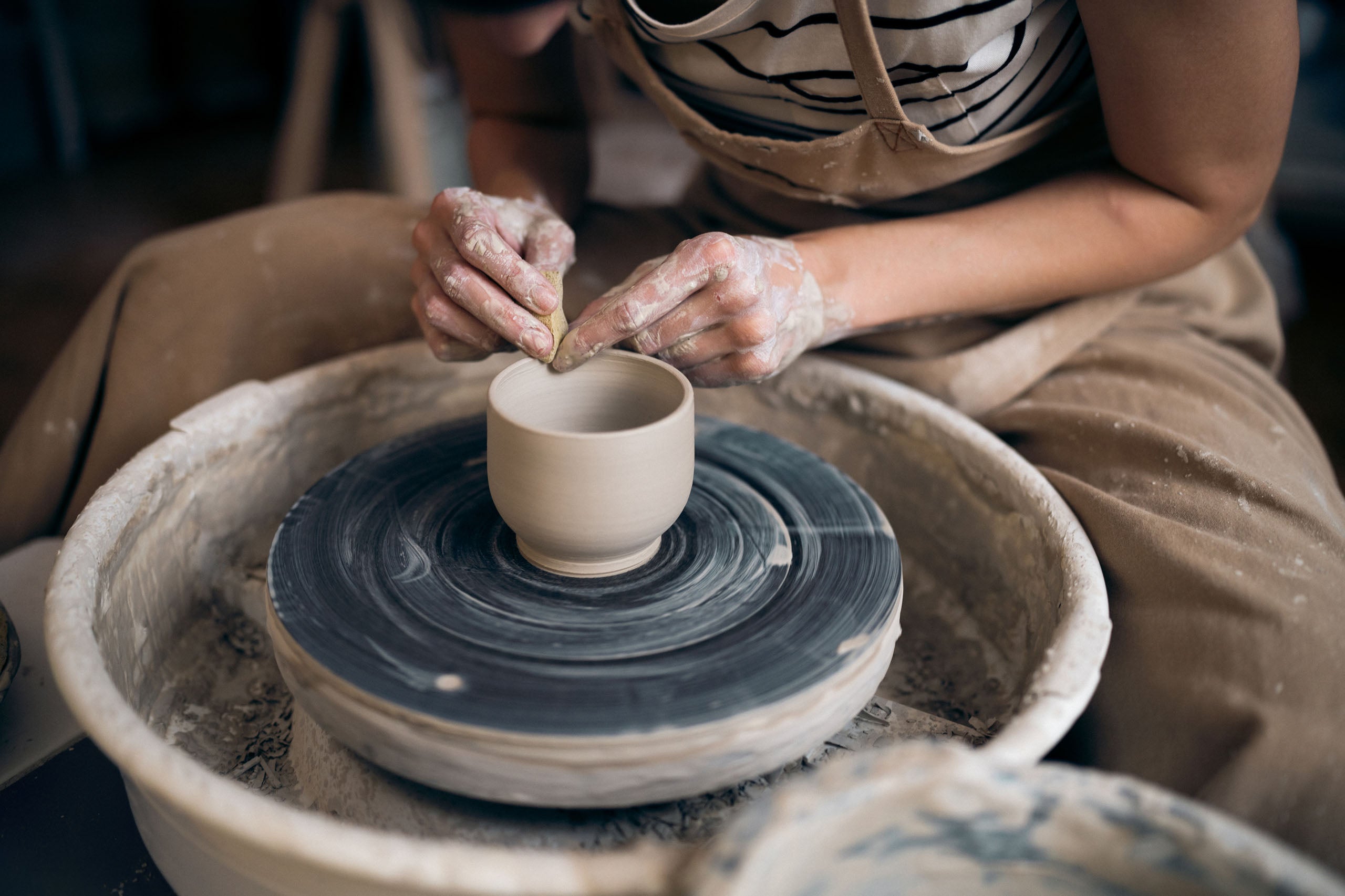 Craftsman shaping a ceramic cup on a potter's wheel.