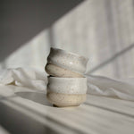 A stack of handcrafted cappuccino cups in speckled white finish, illuminated by contrasting light and shadows.