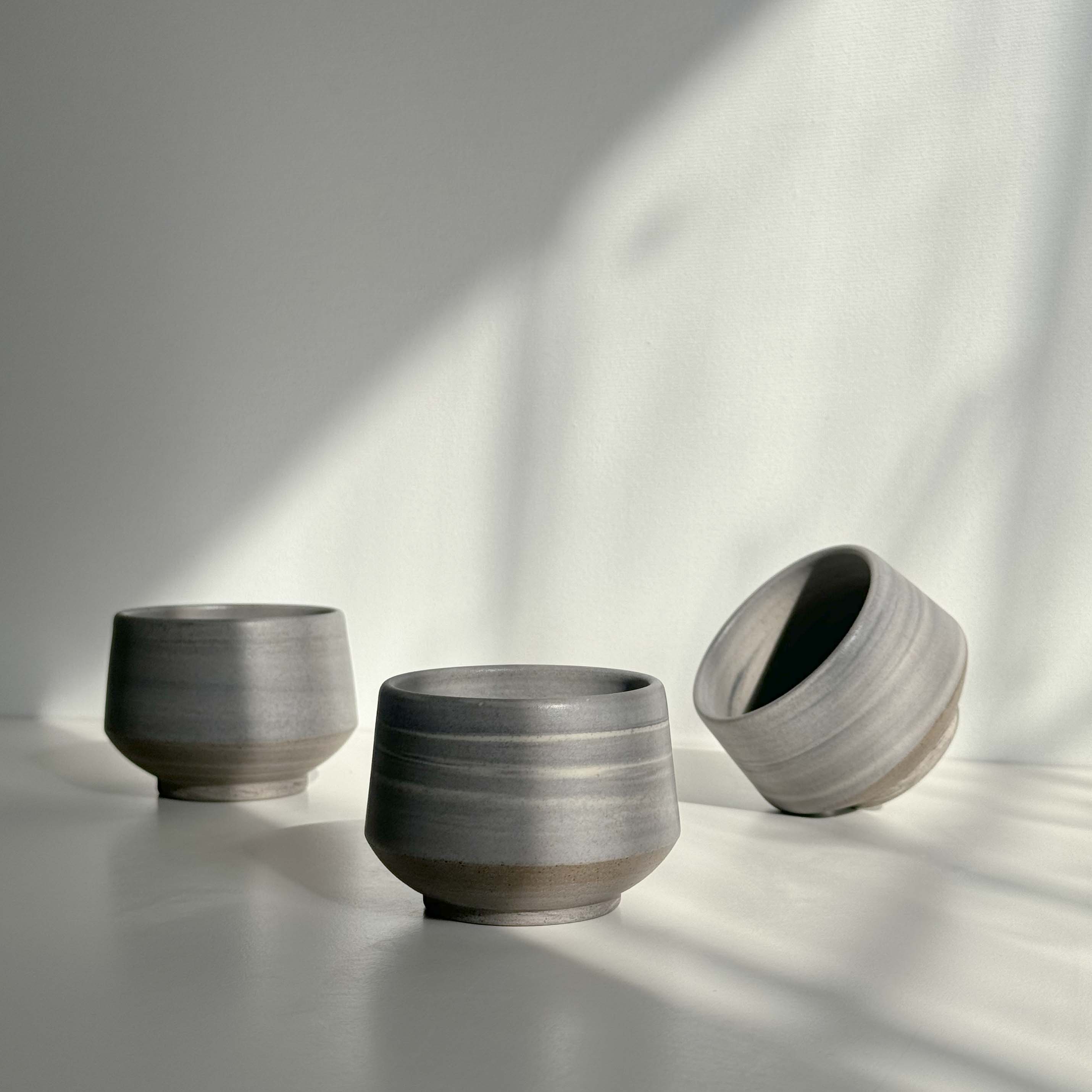 Handcrafted espresso ceramic cups scattered on a white surface.