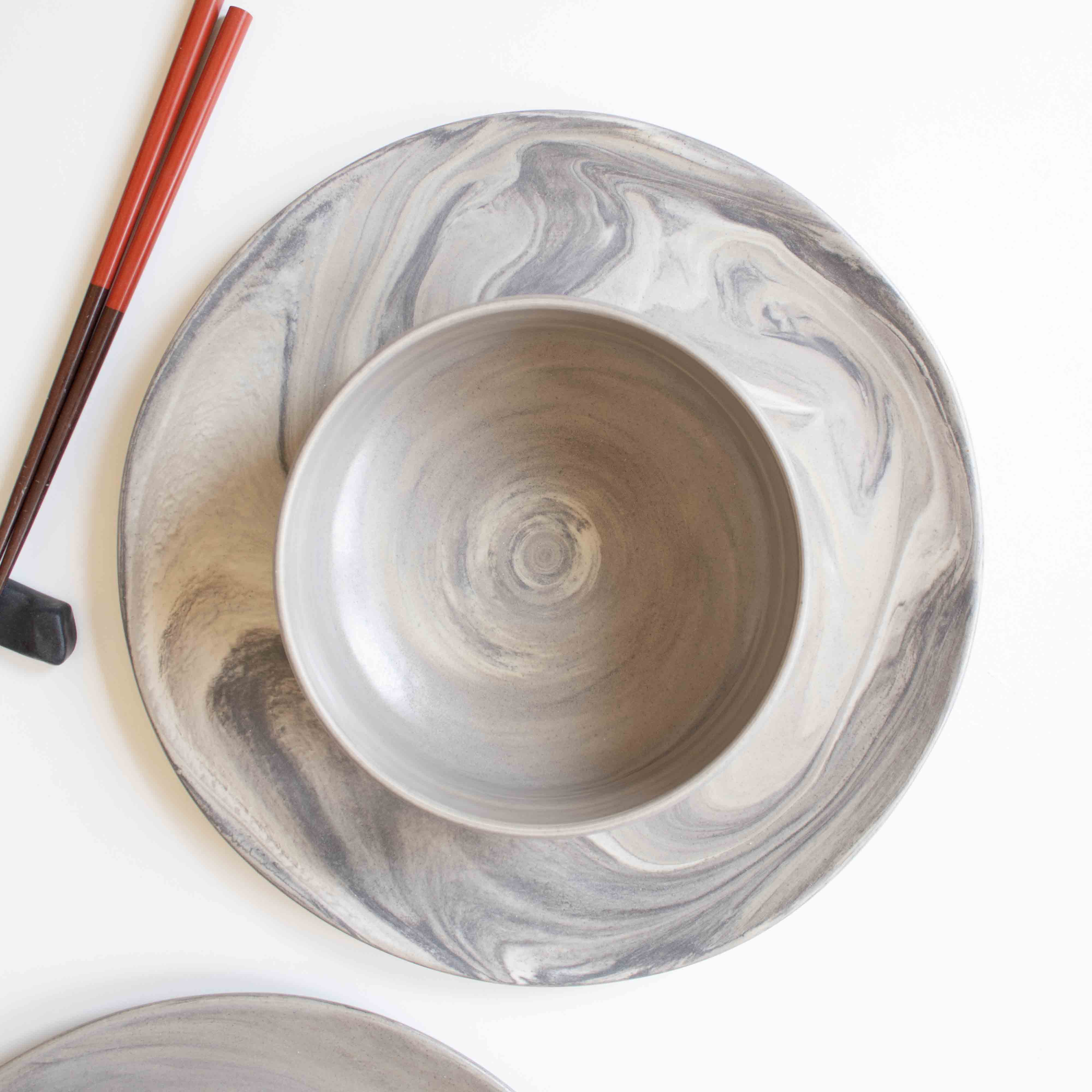 A set of handcrafted marbled ceramic plate, bowl, and chopsticks arranged neatly on a white surface.