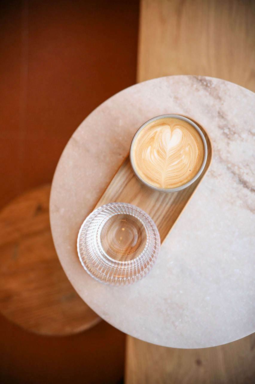 Overhead view of a round marble table with a coffee cup featuring latte art and a glass of water.