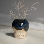 Close-up of a handcrafted ceramic vase with a dark blue finish, holding dried branches, photographed in natural daylight.