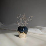 Handcrafted ceramic vase in dark blue finish, containing dried branches, captured in natural daylight.