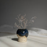 Handcrafted ceramic vase in dark blue finish, containing dried branches, captured in natural daylight.