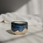 Close-up of a handcrafted ceramic cup made of speckled cream clay, featuring rich melting glaze details in blue.