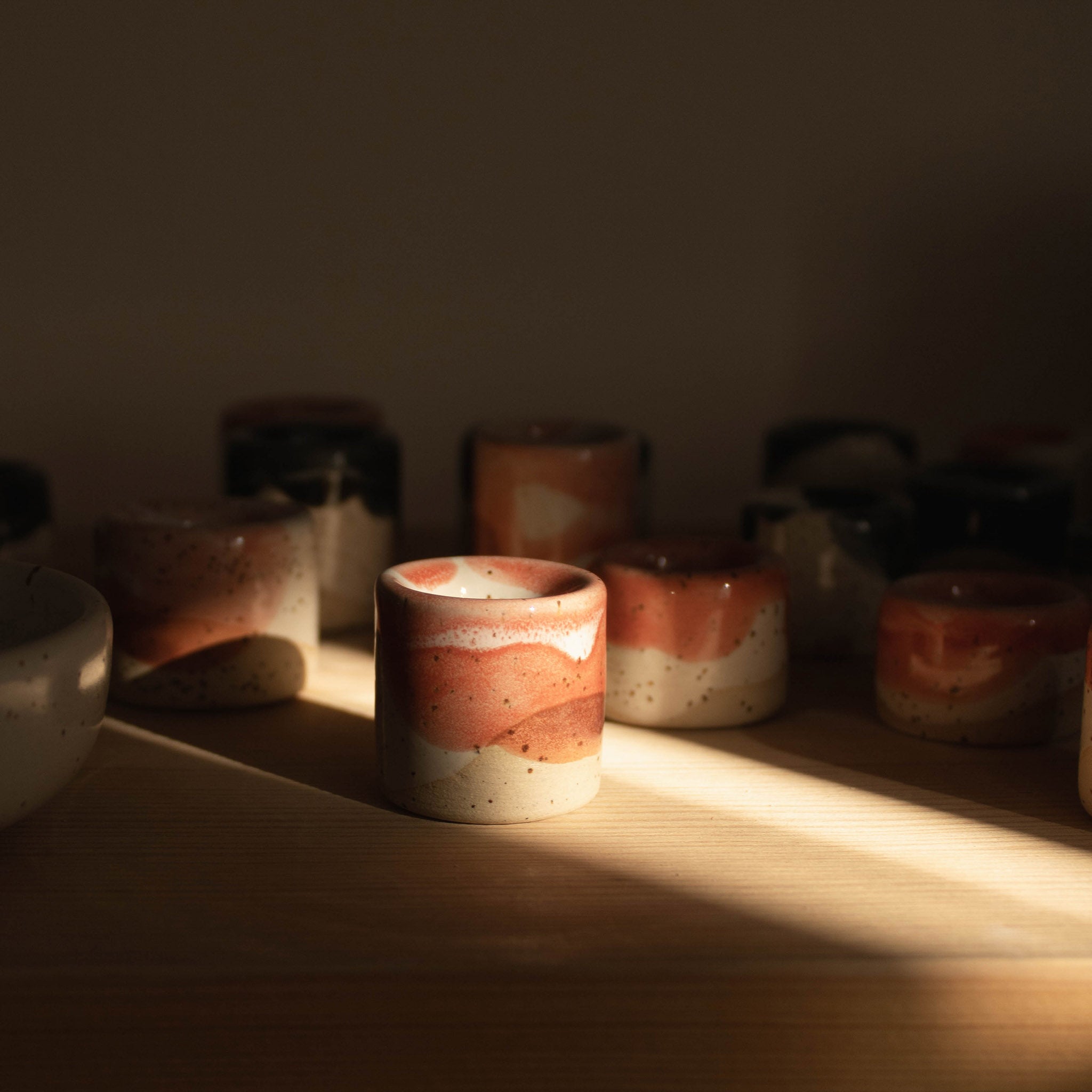 Handmade ceramic pen holder with a coral red finish showcased on a wooden shelf, illuminated by a sharp beam of light.