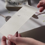 Person filling in a gift voucher and placing it into a decorative envelope with care.