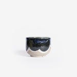 Handmade ceramic cappuccino cup crafted from speckled cream clay, adorned with an organic deep blue and white glaze pattern, captured against a white backdrop.