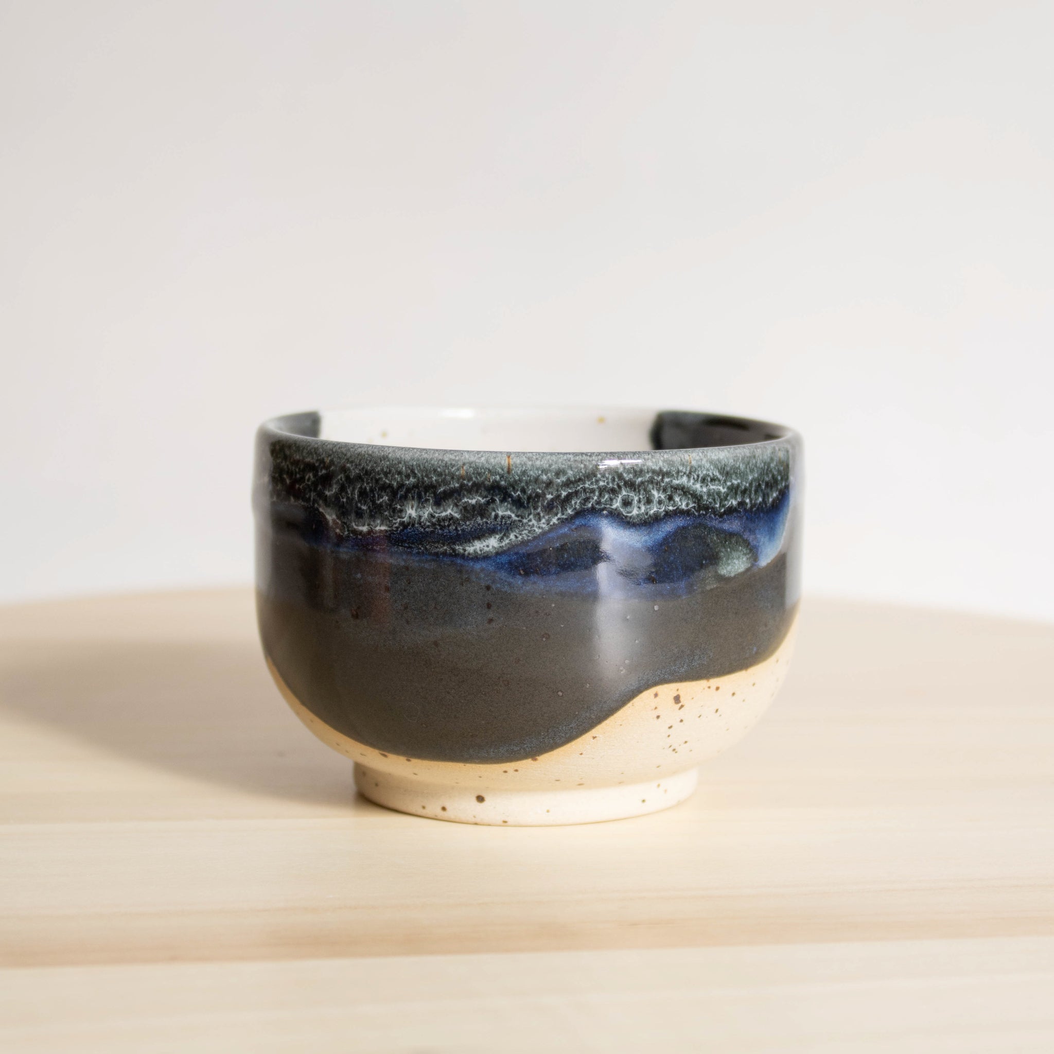 Close-up of a handcrafted ceramic cappuccino cup, emphasizing the striking contrast between its midnight blue and white finish against the matte speckled cream clay of the unglazed bottom.