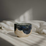 Close up of a handcrafted ceramic cup made of speckled cream clay, featuring rich melting glaze details in blue.